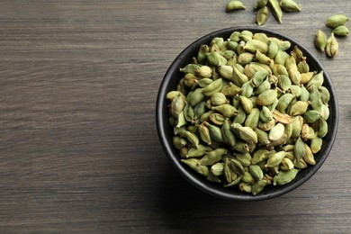 Photo of Bowl of dry cardamom pods on wooden table, top view. Space for text