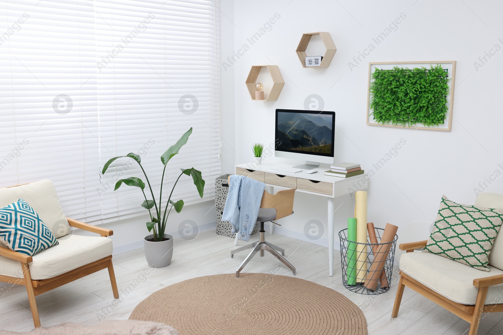 Photo of Green artificial plant wall panel and desk with computer in light room. Interior design