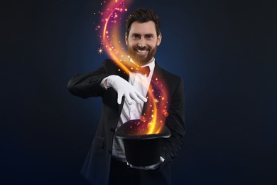Image of Smiling magician showing trick with top hat on dark blue background