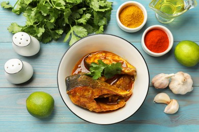 Photo of Tasty fish curry and ingredients on light blue wooden table, flat lay. Indian cuisine