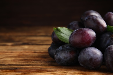 Delicious ripe plums on wooden table, closeup. Space for text