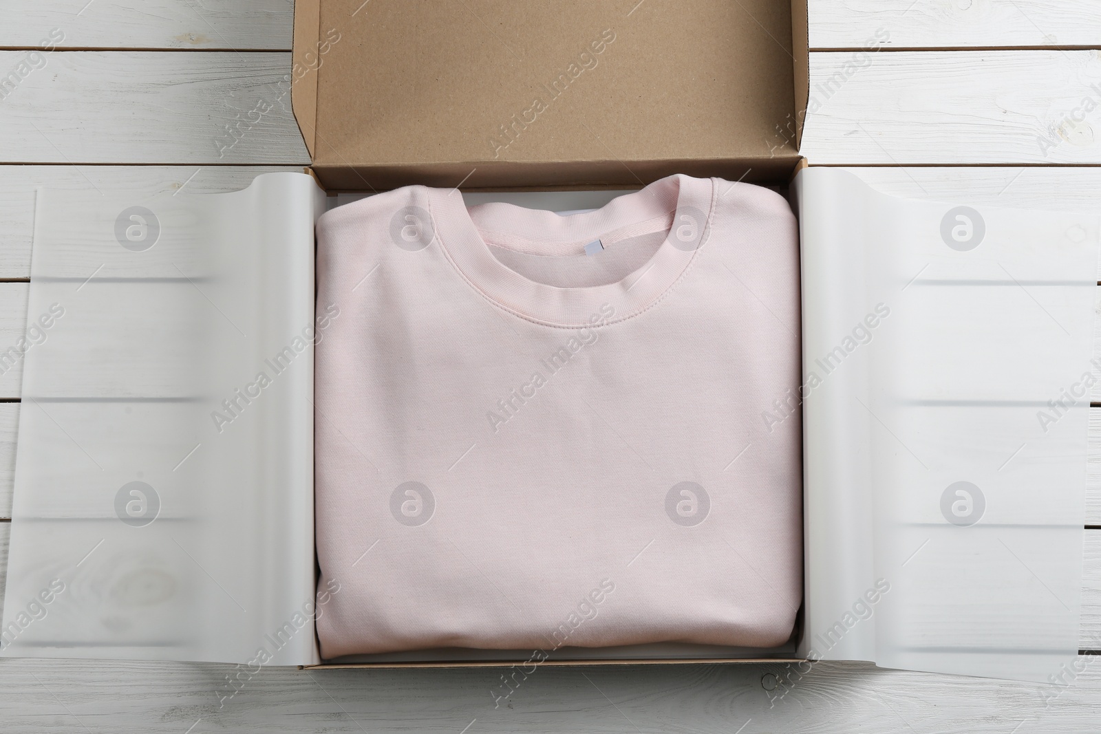 Photo of Cardboard box with clothes on white wooden background, top view