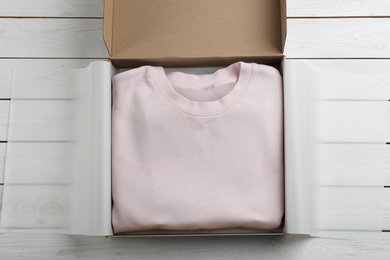 Photo of Cardboard box with clothes on white wooden background, top view