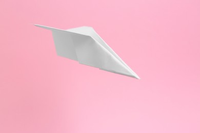 Photo of White paper plane flying on pink background, space for text