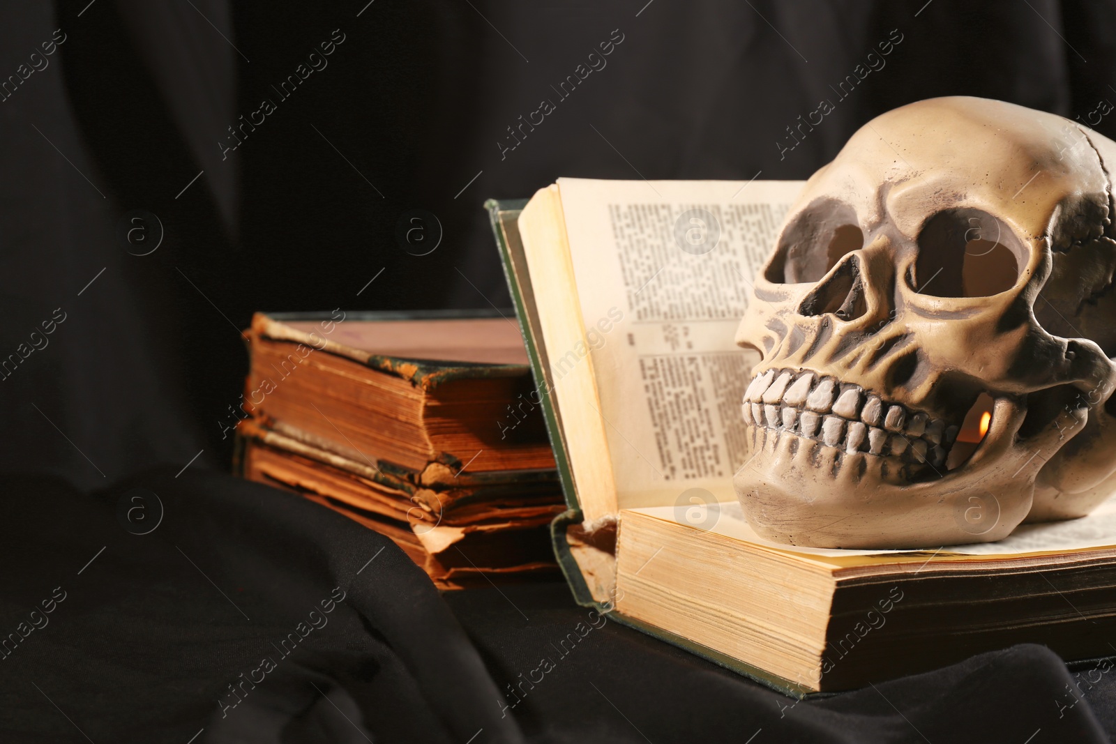 Photo of Human skull and old books on black background. Space for text