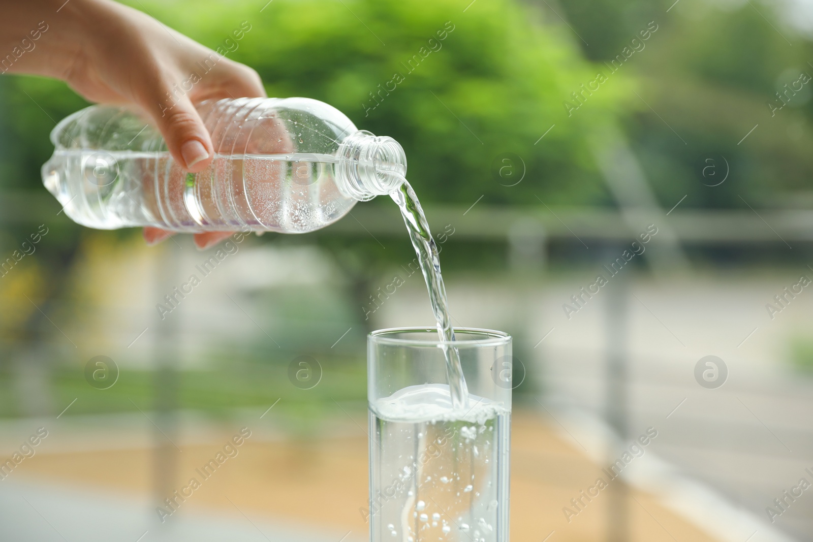 Photo of Woman pouring water from bottle into glass against blurred background, closeup