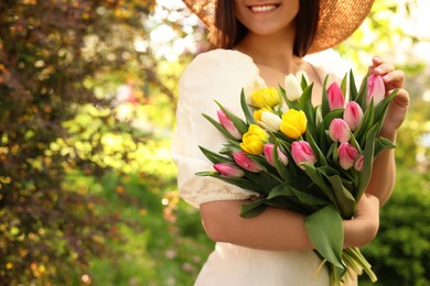 Photo of Young woman with bouquet of tulips in park on sunny day, closeup. Space for text