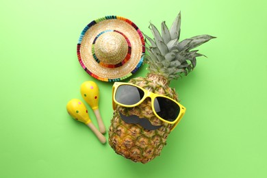 Photo of Mexican sombrero hat, pineapple with sunglasses, fake mustache and maracas on green background, flat lay