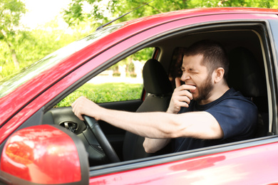 Tired man yawning while driving his modern car