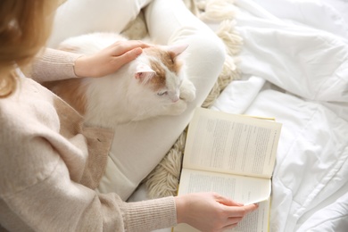 Photo of Woman with cute fluffy cat and book on bed, top view