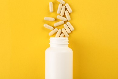 Bottle and vitamin capsules on yellow background, top view