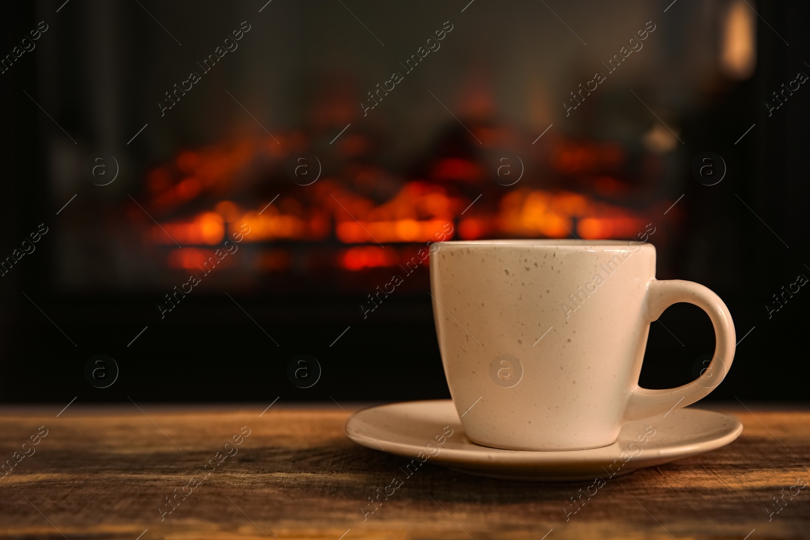 Photo of Cup with hot drink on table against fireplace, space for text