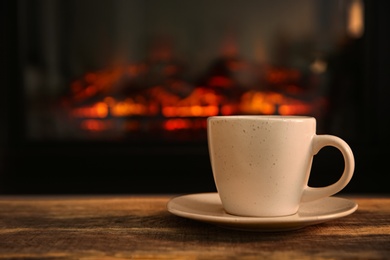 Photo of Cup with hot drink on table against fireplace, space for text