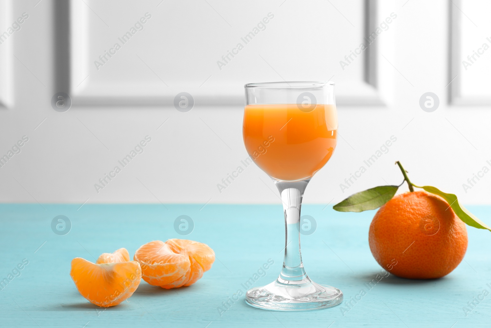 Photo of Delicious tangerine liqueur and fresh fruits on light blue wooden table, space for text