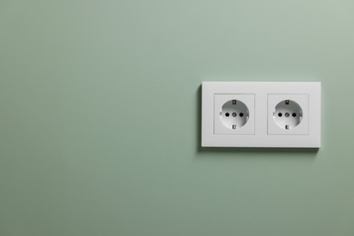Photo of Electric power sockets on light green wall indoors, space for text