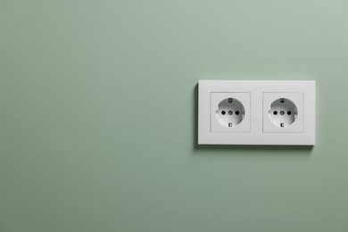 Electric power sockets on light green wall indoors, space for text