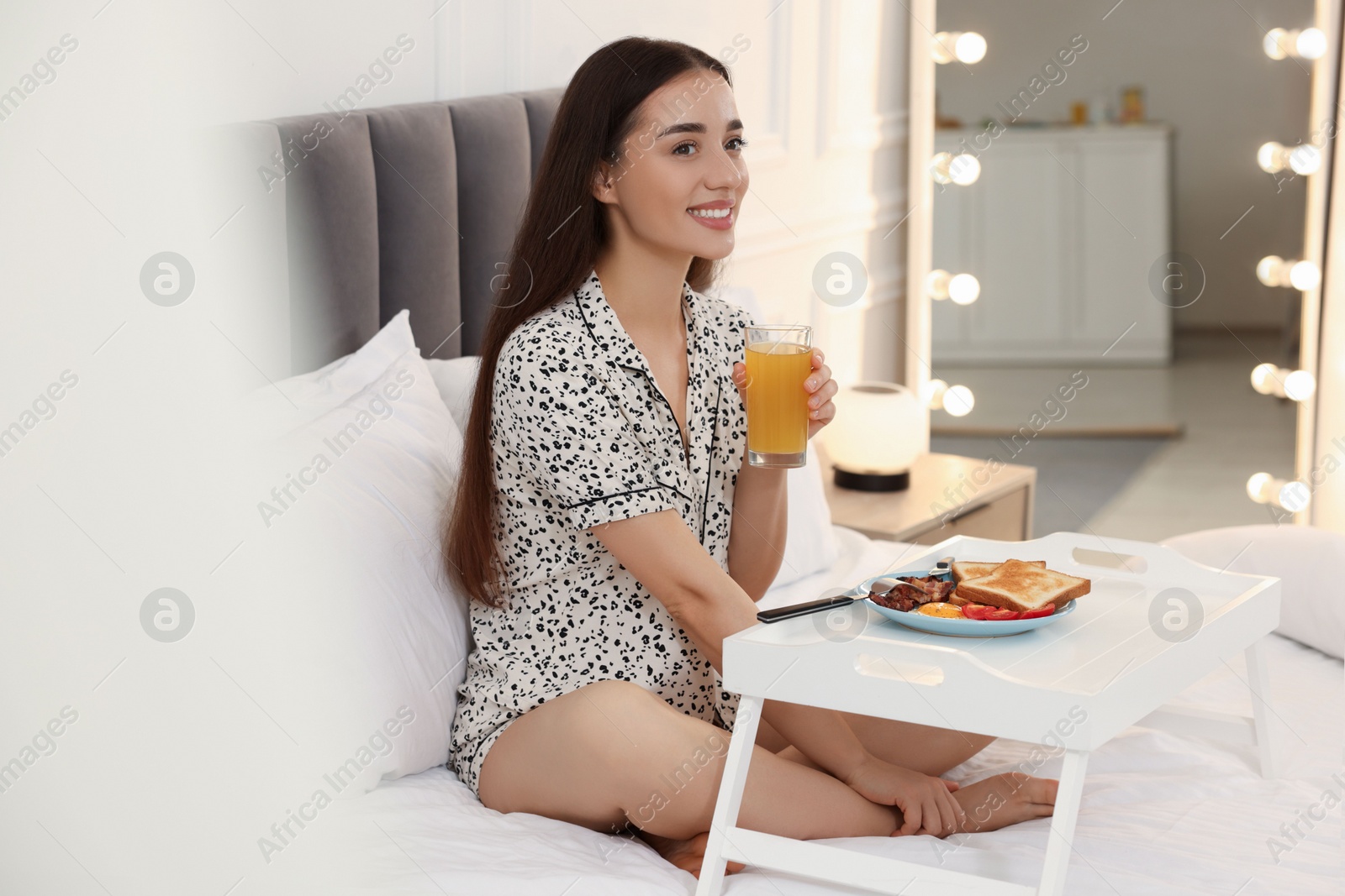 Photo of Happy young woman having breakfast on bed at home