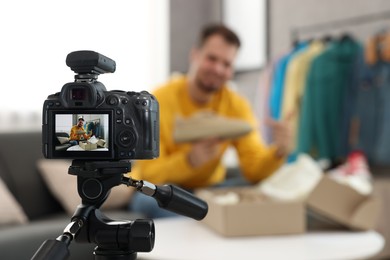 Photo of Fashion blogger showing shoe while recording video at home, focus on camera
