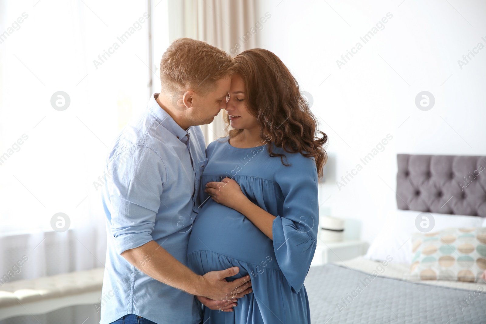 Photo of Pregnant woman with her husband in bedroom. Happy young family