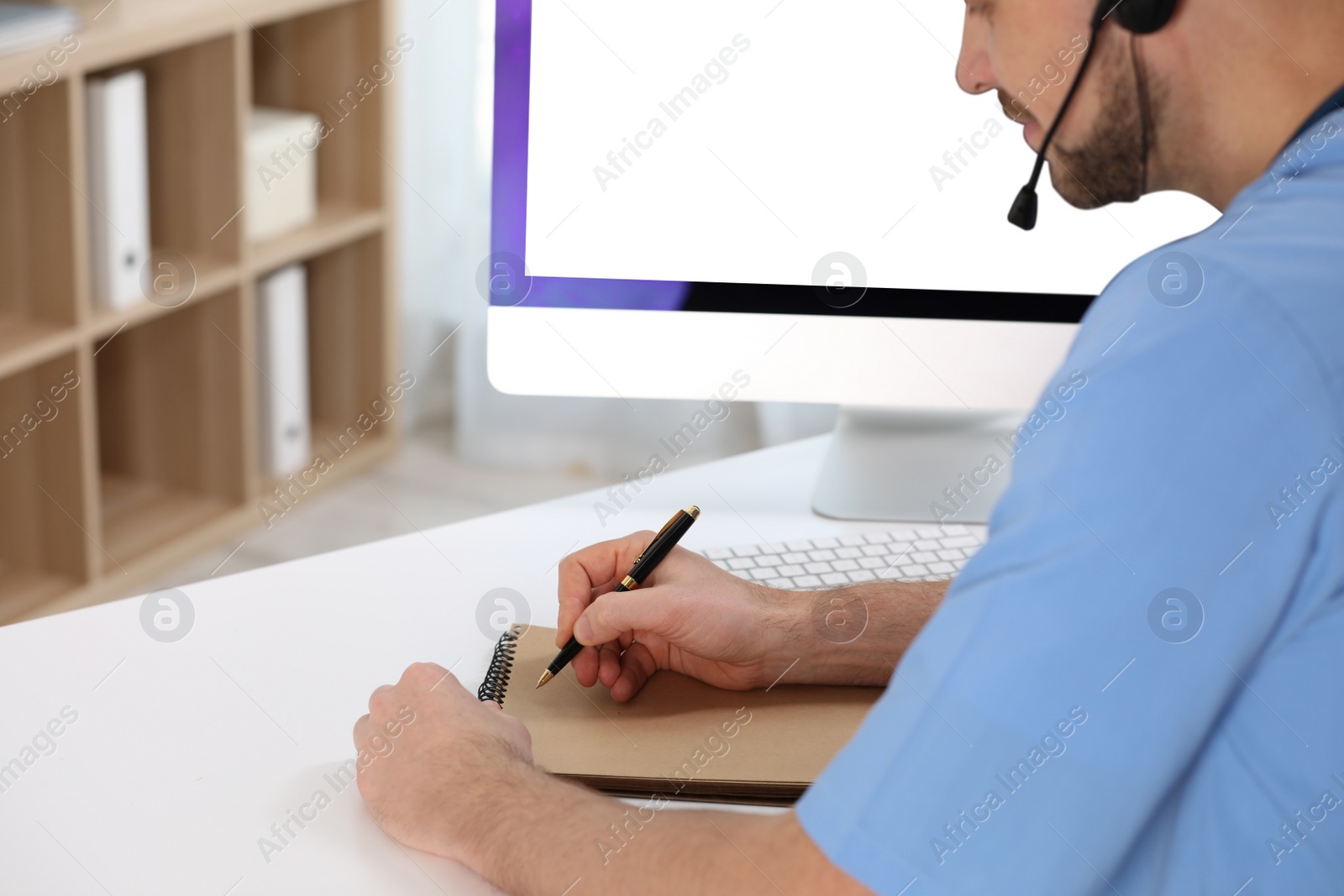 Photo of Doctor with headset consulting patient online at desk in clinic. Health service hotline