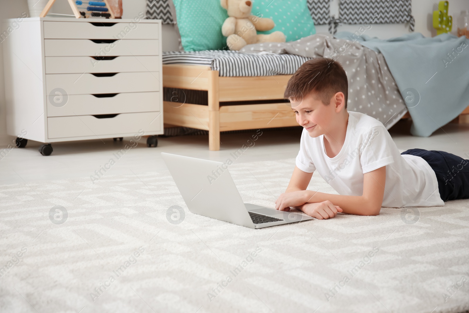 Photo of Happy boy with laptop lying on cozy carpet at home