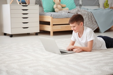 Happy boy with laptop lying on cozy carpet at home