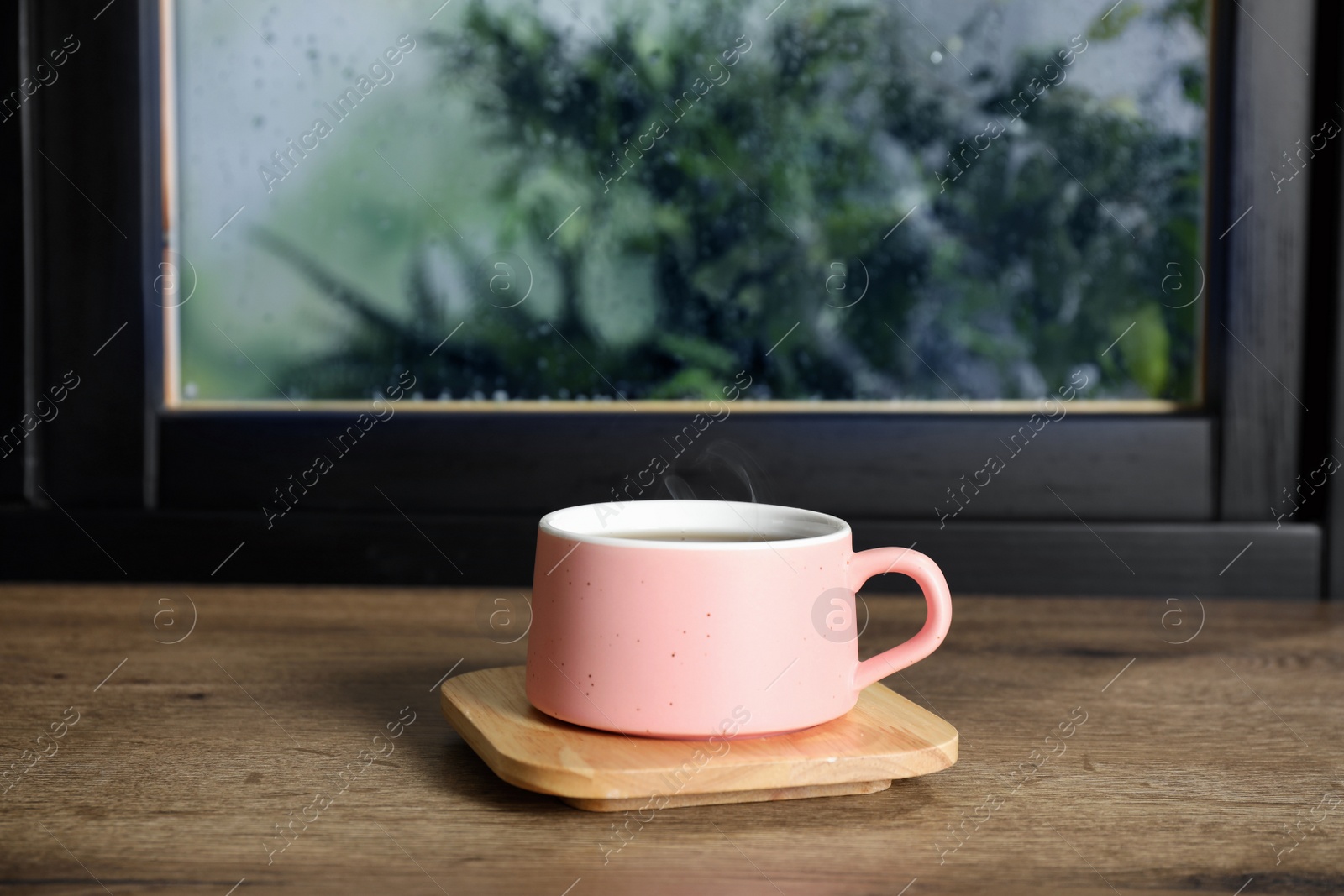 Photo of Cup of hot drink on window sill against glass with rain drops, space for text