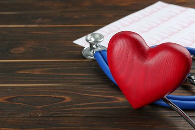 Photo of Stethoscope and red heart on wooden table, closeup with space for text. Cardiology concept