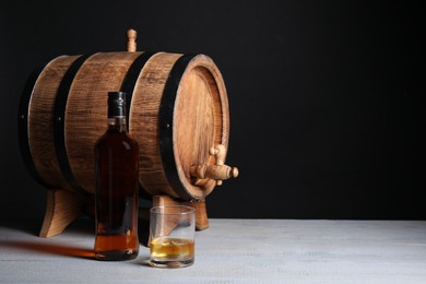 Photo of Barrel with tap, bottle and glass of tasty whiskey on light gray wooden table, space for text