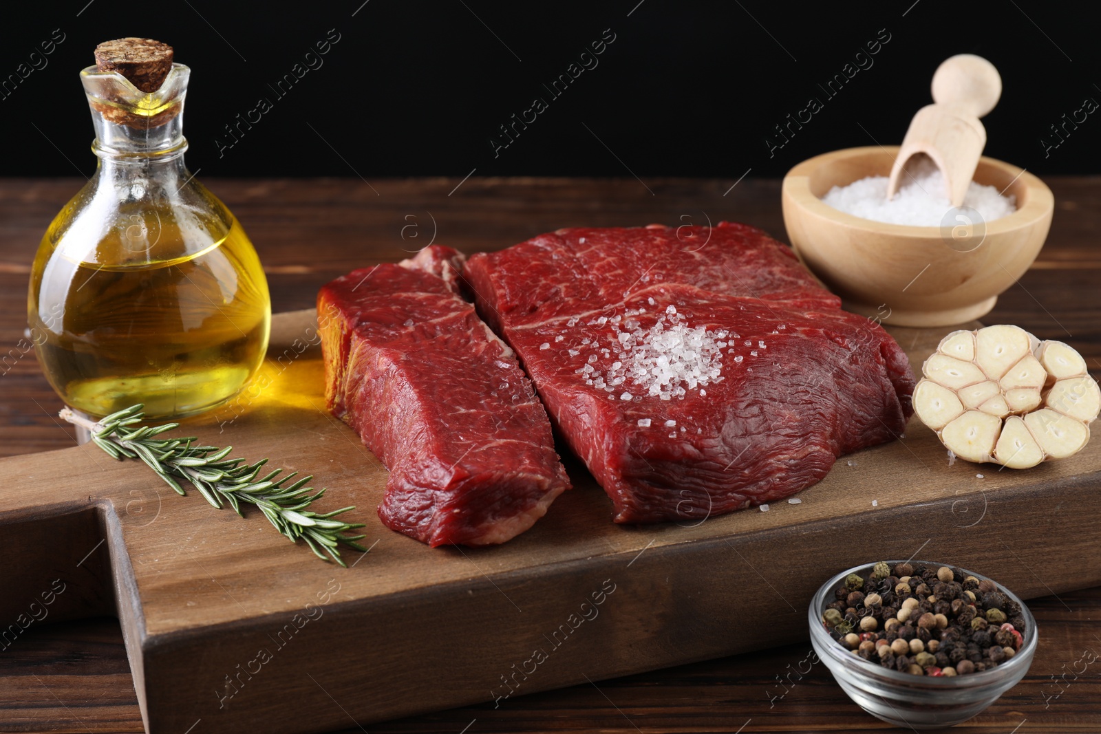 Photo of Fresh raw beef cuts with oil and spices on wooden table