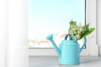 Photo of Watering can with lily of the valley bouquet on windowsill, space for text