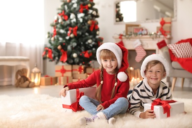 Cute little children in Santa hats with Christmas gift boxes at home