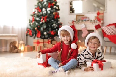 Photo of Cute little children in Santa hats with Christmas gift boxes at home