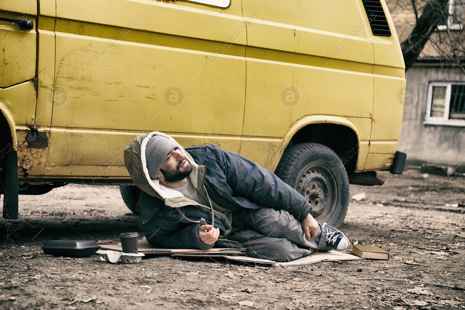 Photo of Poor homeless man lying near van outdoors