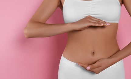 Woman in underwear holding something near her belly on pink background, closeup. Healthy stomach