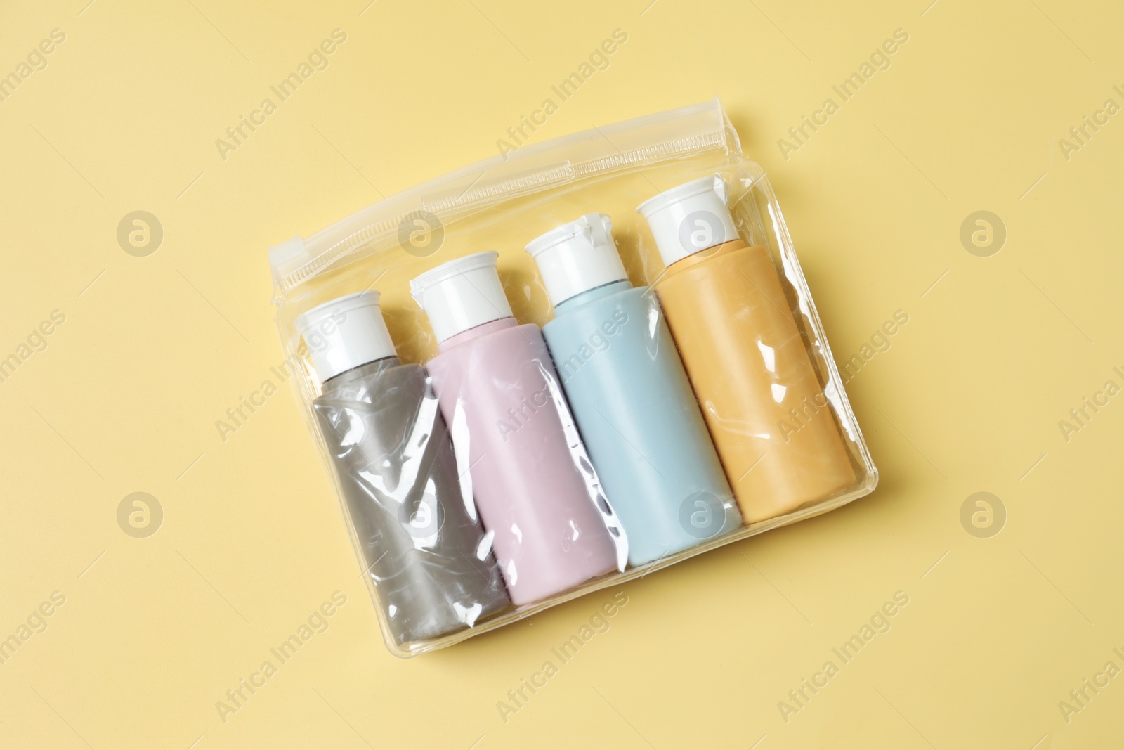 Photo of Cosmetic travel kit in plastic bag on yellow background, top view