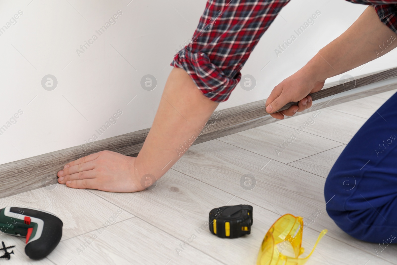 Photo of Man installing plinth on laminated floor in room, closeup