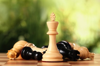 Wooden king among fallen chess pieces on game board against blurred background, closeup
