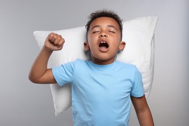 Photo of Boy with pillow yawning and stretching on grey background. Insomnia problem