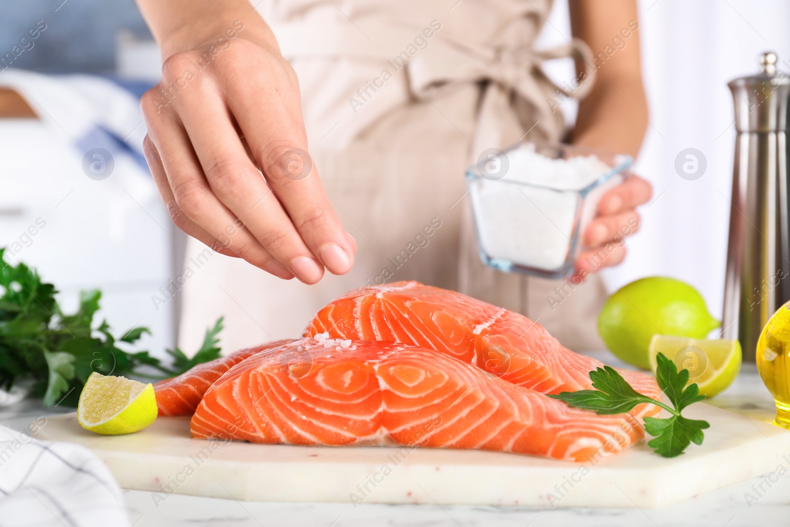 Photo of Woman salting fresh raw salmon at table, closeup. Fish delicacy