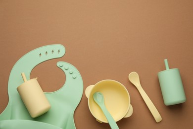 Photo of Flat lay composition with baby feeding accessories and bib on brown background, space for text