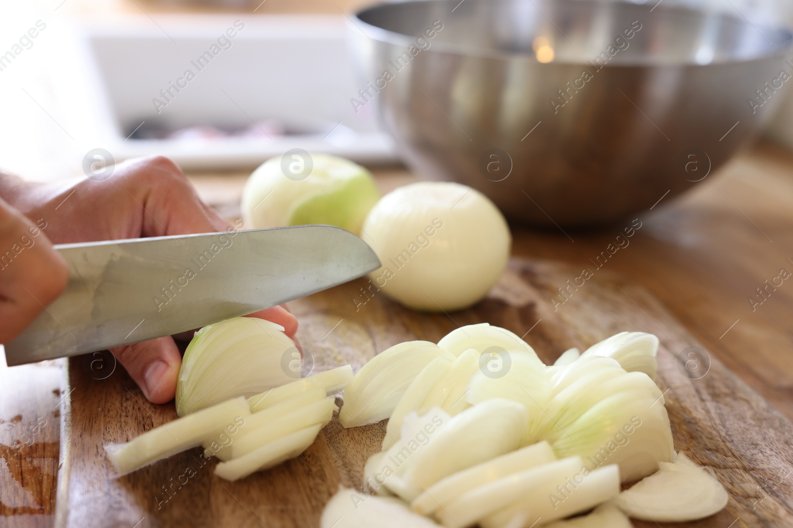 Photo of Woman cutting fresh ripe onion on wooden board, closeup