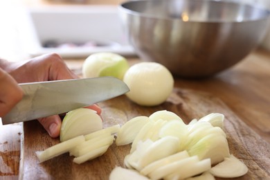 Photo of Woman cutting fresh ripe onion on wooden board, closeup