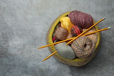 Photo of Soft woolen yarns and knitting needles on grey table, top view. Space for text