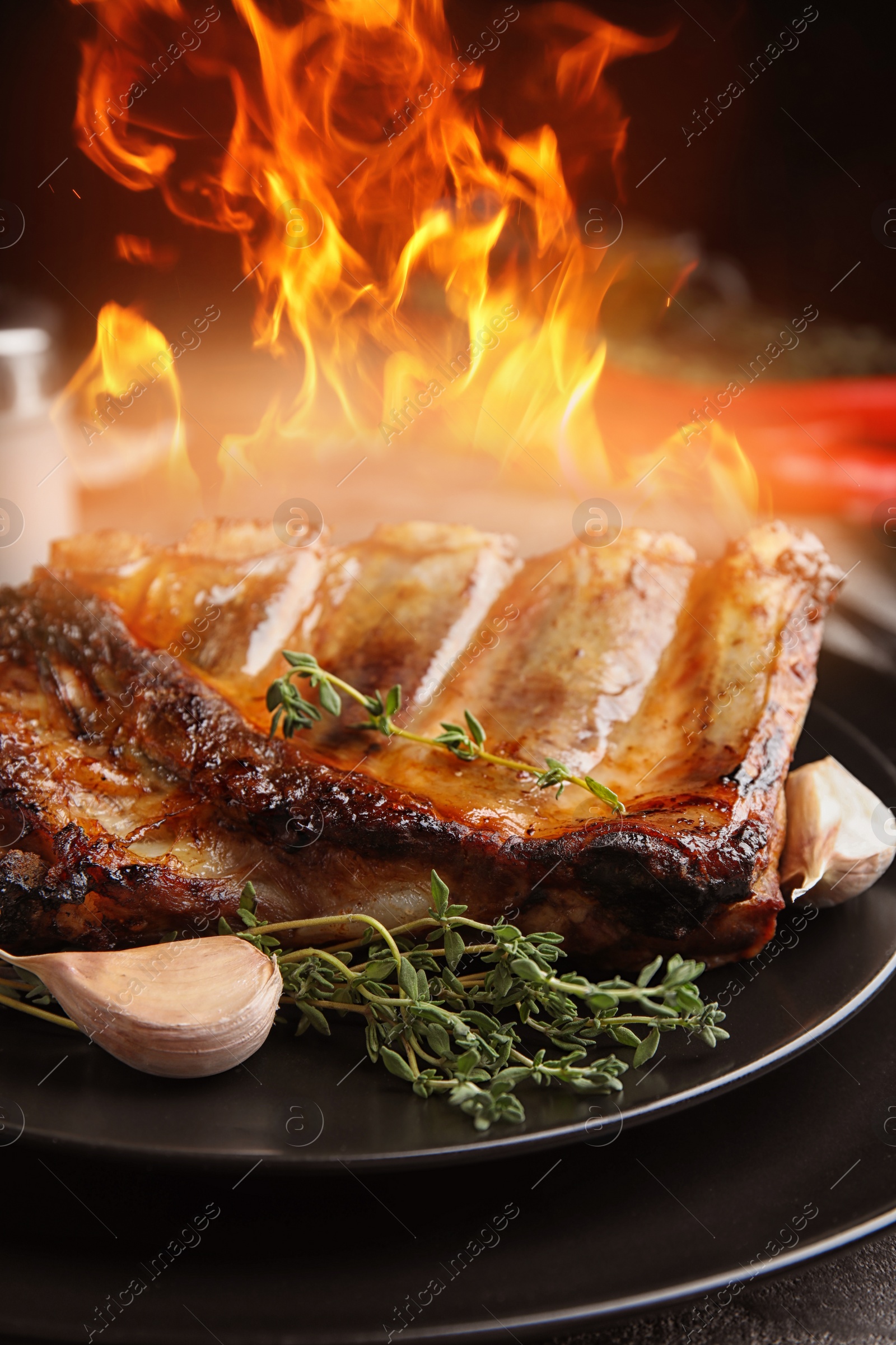 Image of Tasty grilled ribs and flame on plate, closeup