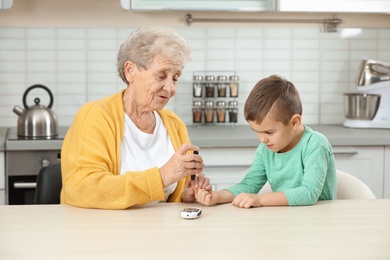 Photo of Senior woman with her grandson using lancet pen at home. Diabetes control