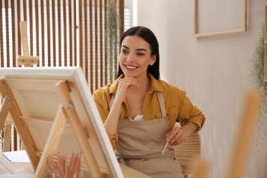 Photo of Young woman drawing on easel with pencil at table indoors