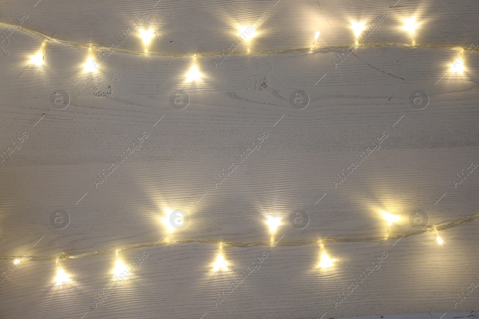 Photo of Frame of beautiful glowing Christmas lights on white wooden table, top view. Space for text