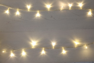 Photo of Frame of beautiful glowing Christmas lights on white wooden table, top view. Space for text