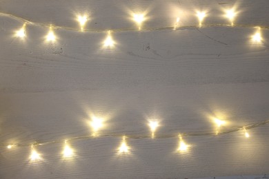 Frame of beautiful glowing Christmas lights on white wooden table, top view. Space for text